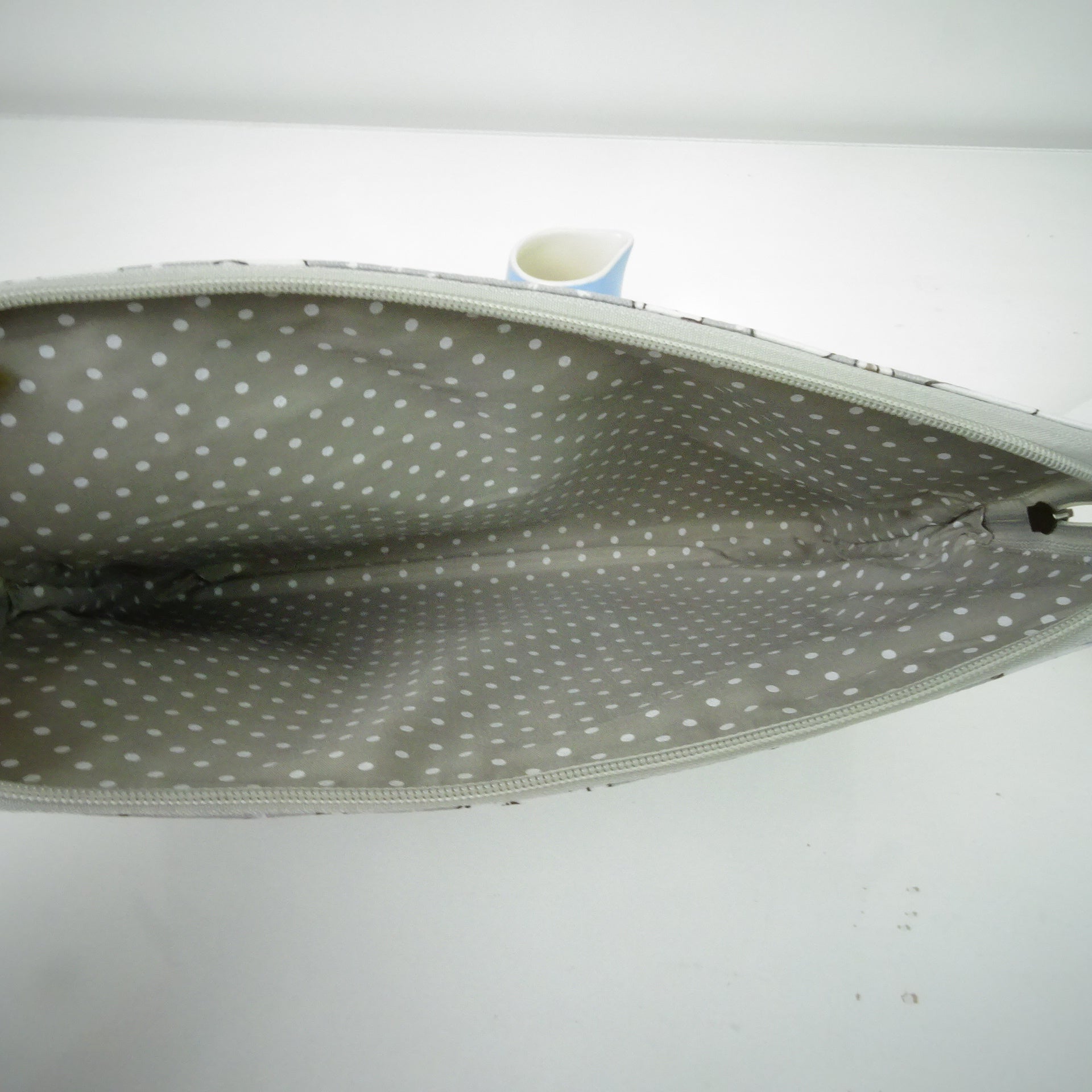 An open zippered pouch or bag showing a gray interior with a white polka dot pattern, photographed against a plain white background.